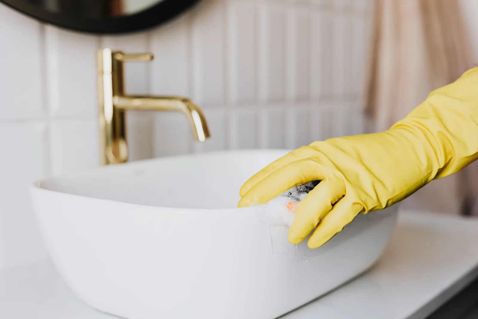 Gloved hand cleaning a bathroom sink